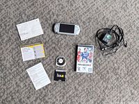 Overview of all items laid out on floor: PSP console, power adapter, three UMDs, manuals