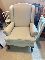 Front view of beige/cream wingback chair with dark wood legs and removable cushion