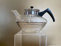 Full side view of glass teapot showing silver stripes, handle, spout and lid