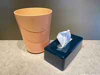 Peach wastebasket and dark teal tissue box cover on countertop