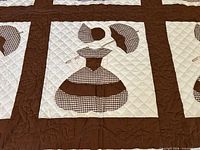 Close-up of a Sunbonnet Sue appliqué block showing brown gingham fabric, cream background, and decorative hand quilting.