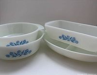 Group of four milk glass dishes showing two round casseroles, one rectangular baker, and one oval divided dish