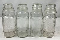 Front view of four clear glass Mr. Peanut canisters, two with stoppers
