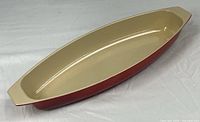 Full view of red exterior and cream interior oval au gratin pan