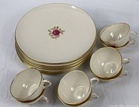 Stack of eight dinner plates with four cups showing pattern and gold trim