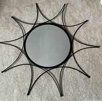 Front view of round mirror with starburst black metal frame on carpet