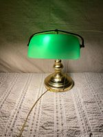 Front view of brass banker’s lamp showing base, green shade, pull chain and cord