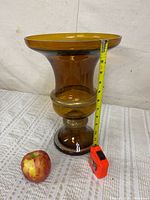 Full view of amber glass vase beside tape and apple, showing height