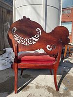 Full rear view of carved wooden chair with red velvet seat.