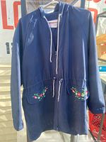 Full view of navy anorak showing hood, drawstring waist and embroidered pocket flaps