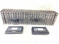 Front view of 30 VHS tapes in cases, two stacks of loose tapes