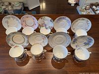 Nine teacups paired with nine saucers displayed upright on wooden surface