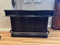 Front view of dark wood bar with paneled design and metal foot rail