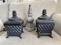 Front view of two black lidded boxes and grey finial on couch