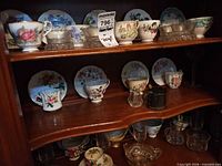Two cabinet shelves with bone china teacup and saucer sets in various floral patterns, silverplate holders and cups visible