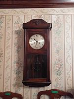 Front view of Kienzle wall clock hanging on wall showing full case, dial and glass panel