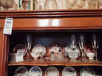 Cabinet shelf showing bone china teacups with saucers, pressed glass shakers and glass flutes