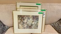 Three framed floral watercolors stacked on sofa