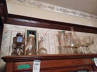 Group of clear and amber glass items on cabinet top: oil lamps, decanter, vases, stemware