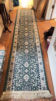 Full length view of green and ivory oriental runner rug with fringe