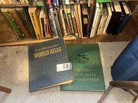 Two large atlases on floor plus bookshelves behind