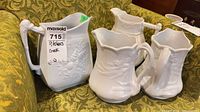 Front view of four white ironstone pitchers on green fabric
