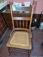 Full view of wooden armless rocking chair showing front, carved crest rail, spindle back, cane seat, rockers