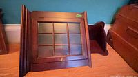 Front view of wooden corner wall cabinet showing glass door with nine-pane mullions and brass knob