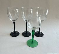 Front view of four stemmed wine glasses showing three black-stemmed and one green-stemmed