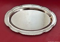 Full view of oval silver-tone tray showing ornate rim and etched center