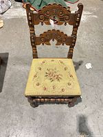 Front view showing carved back splats, turned stretchers, needlepoint seat