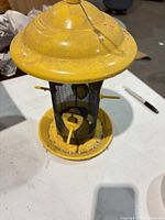Yellow metal mesh bird feeder showing overall form and paint wear