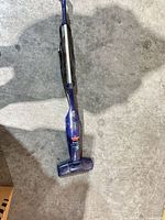 Full view of purple Bissell stick vacuum standing on concrete floor