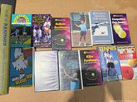 Array of eleven tennis instruction VHS tapes and one yearbook visible
