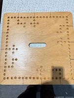 Top view of square wooden cribbage board showing scoring holes and center handle slot
