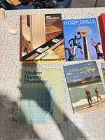 Top view of four books: New Living Spaces, Hoop Drills, Modern Human Physiology, Physical Fitness: A Way of Life