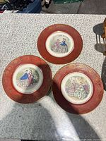 Three red-rimmed Victorian scene plates
