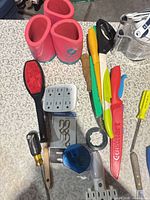 Assortment of knives, silicone grips, cube tap, screwdrivers, electrical tape, ceiling hooks, measuring jug