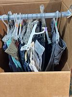 Box with clothing on hangers, various pants and tops visible