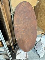 Oval brown wood tabletop lying on edge with visible grain, scratches, hardware holes