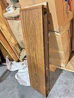 Rectangular brown oak veneer wall shelf standing vertically, showing woodgrain finish and pre-drilled mounting holes