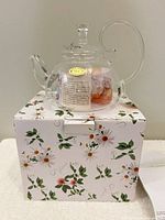 Glass teapot with lid sitting on floral box