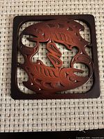Front view of square wooden trivet showing salmon motif