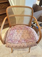 Front view showing cane backrest, curved arms, upholstered seat with patterned cushion