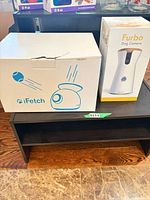 Front view of both boxed items: iFetch launcher and Furbo camera
