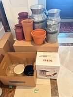 Overall lot showing boxed bird feeder cam, galvanized cans, orange planters, glass vases in carton