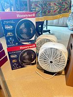 Two boxed Honeywell fans beside two white box fans