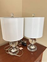 Both matching crystal and chrome lamps with shades on tabletop