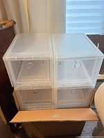 Four assembled clear plastic shoe boxes stacked atop a cardboard box, illustrating quantity and stackability