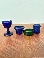 Front view of four glass eye wash cups showing colors and shapes